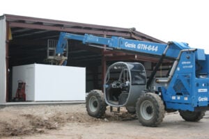 Blue telehandler lifting large white container into building