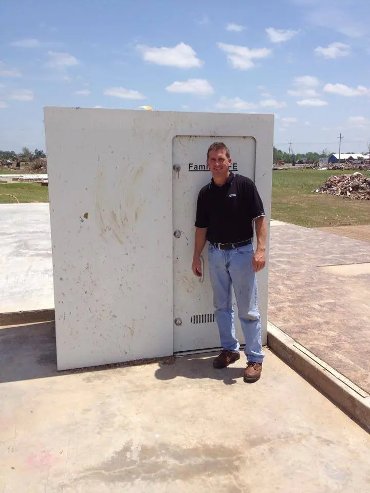 Man standing beside large outdoor storm shelter