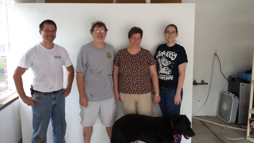 Four adults posing indoors with black dog