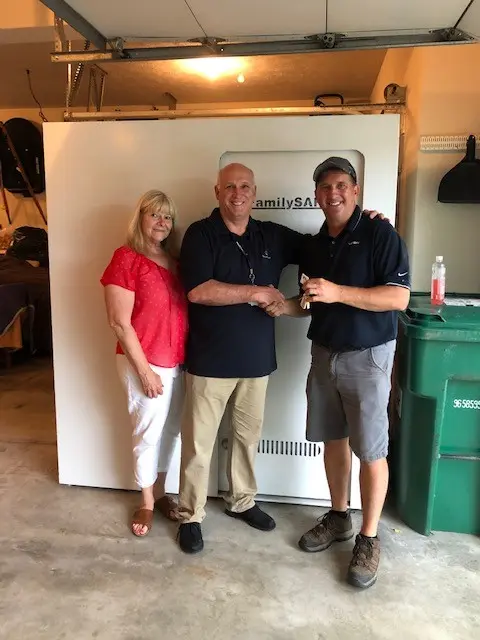 Three adults shaking hands in front of large safe