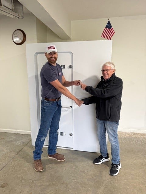Two men holding key in front of safe