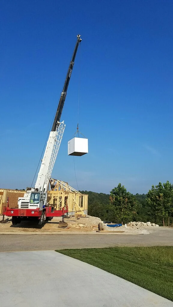 Crane lifting large white unit onto house frame